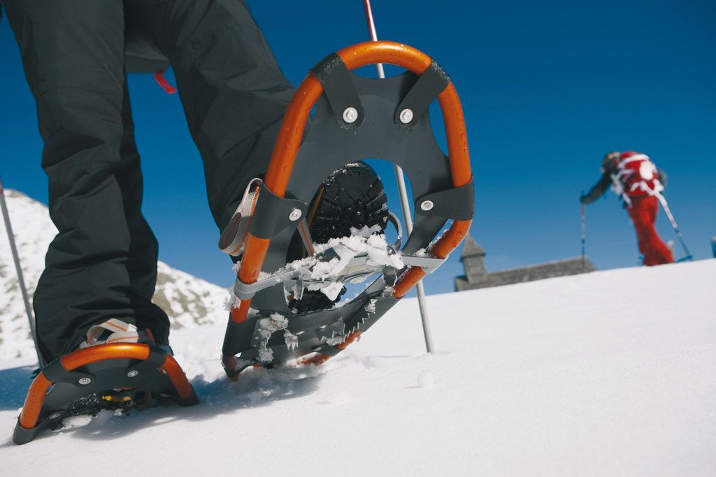 Primo piano di una ciaspola arancione che si solleva dalla neve durante un viaggio di gruppo WeRoad su una montagna soleggiata.