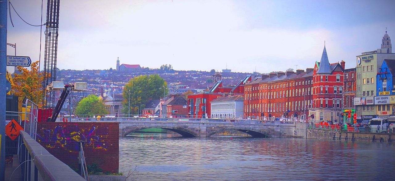 Un puente de piedra con múltiples arcos cruza un río ancho, que conduce a un paisaje urbano con edificios coloridos y una colina al fondo.
