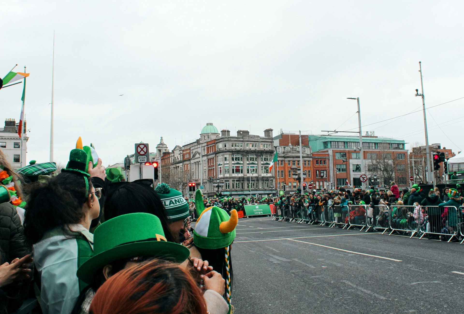 Un voyage de groupe WeRoad observe un défilé derrière des barricades, avec de nombreuses personnes portant des chapeaux verts.