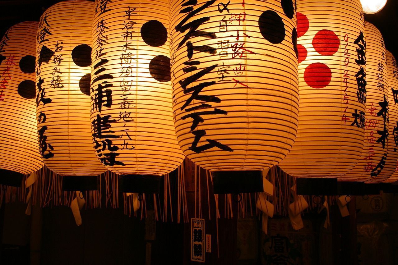 Una fila di lanterne di carta giapponesi illuminate con calligrafia pende nell'oscurità, proiettando un caldo bagliore.