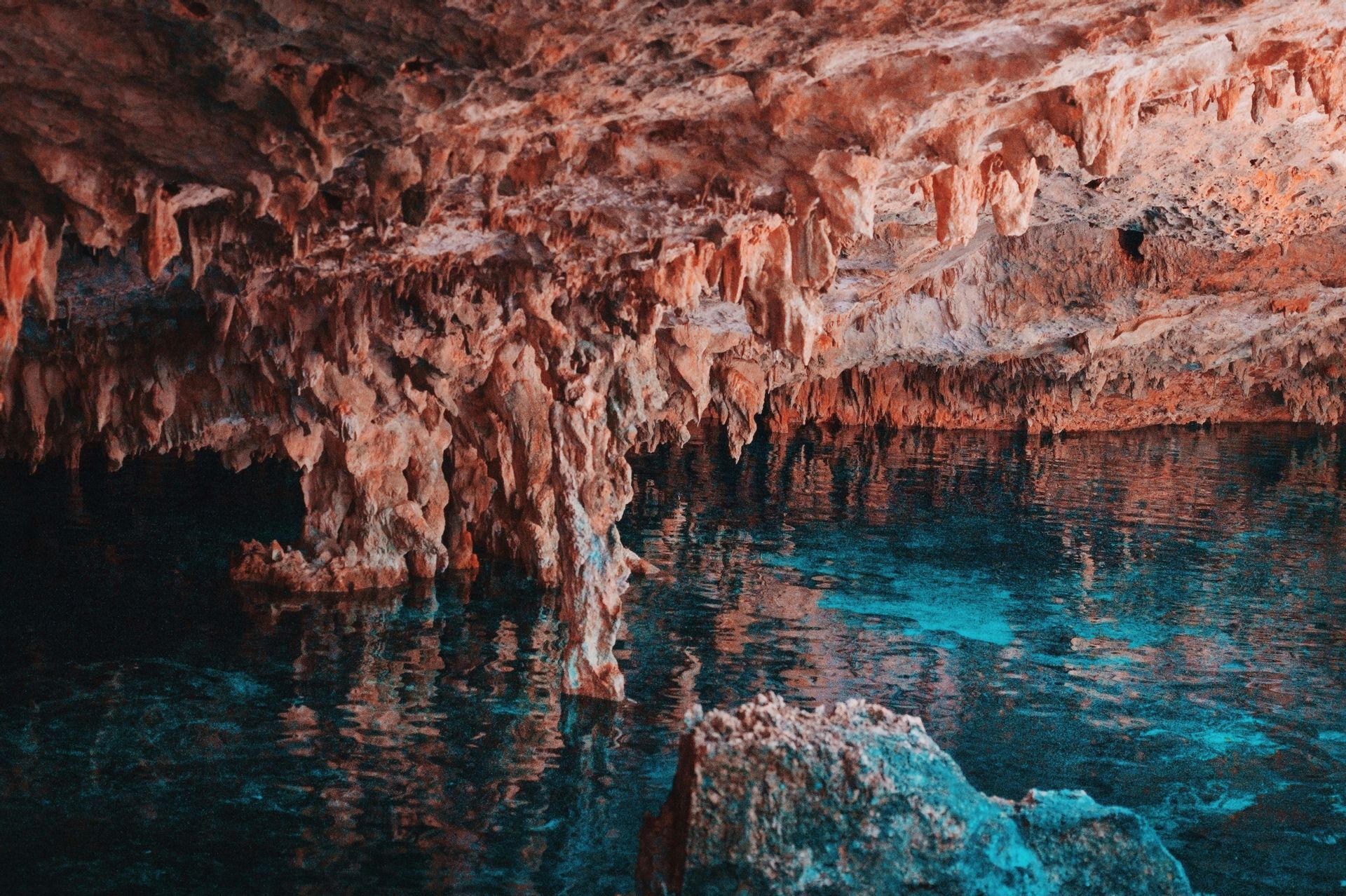 Stalattiti marrone-rossastre pendono sulla superficie di acqua cristallina e turchese all'interno di una grotta sotterranea.