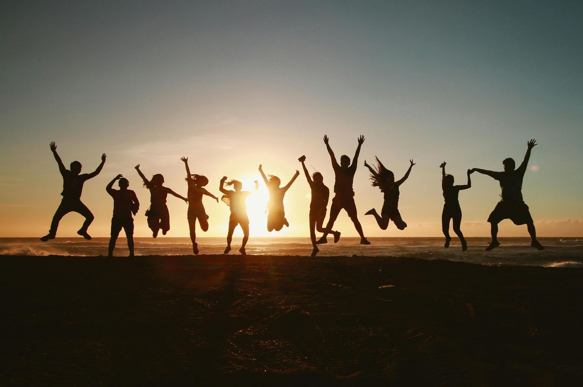 Un viaggio di gruppo WeRoad con persone in silhouette che saltano su una spiaggia al tramonto.