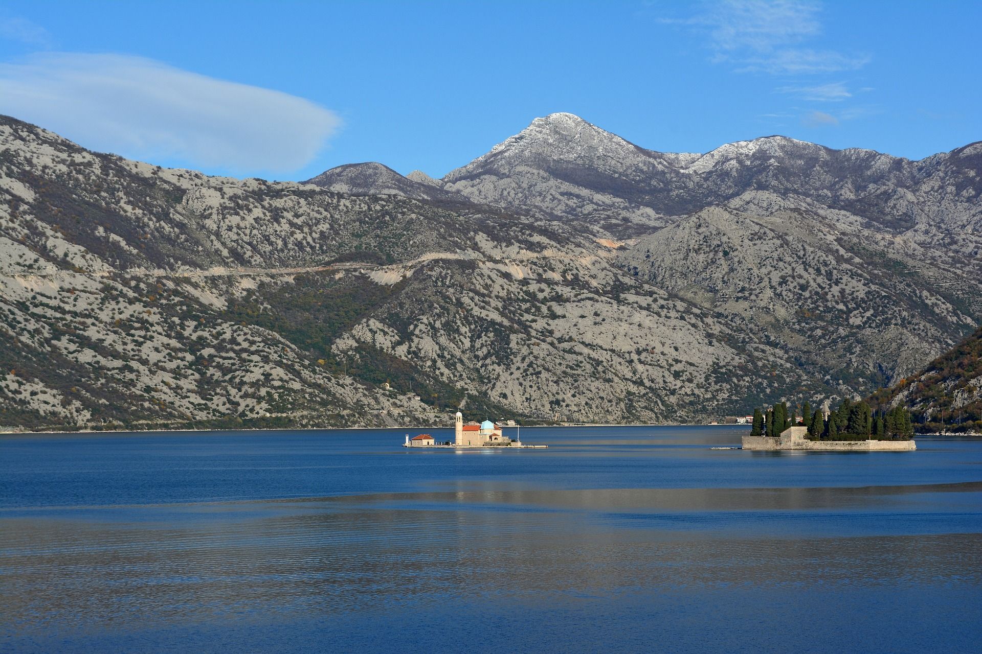 Due piccole isole, una con una chiesa e l'altra con alberi, si trovano su una tranquilla baia blu davanti a una grande catena montuosa rocciosa.