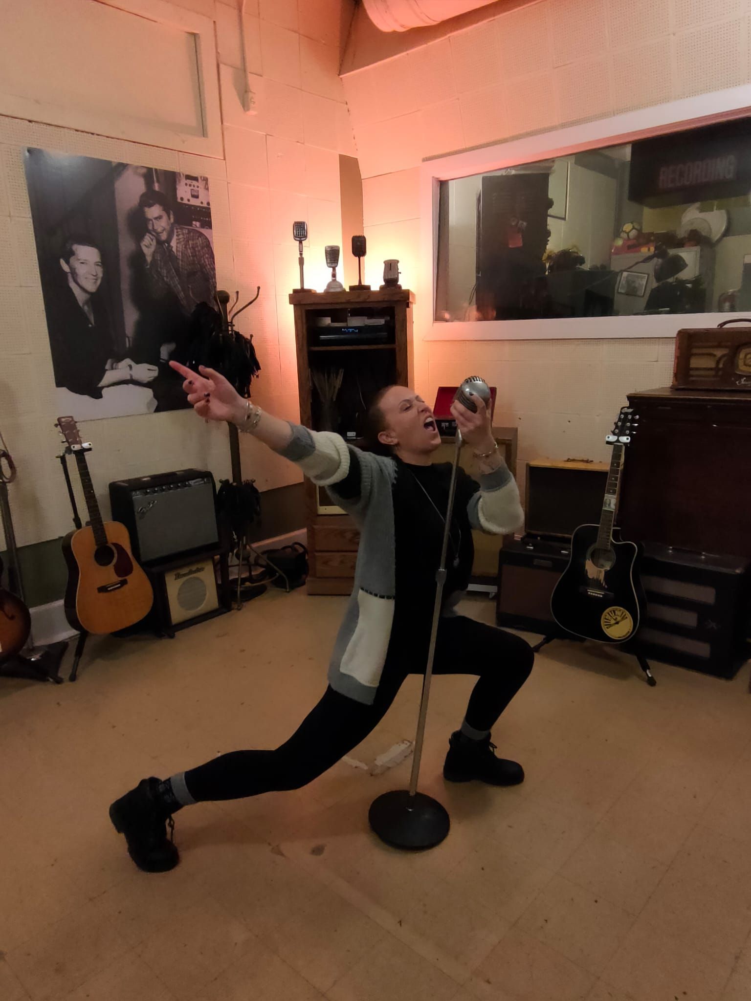 Une personne prend la pose en chantant dans un microphone vintage à l'intérieur d'un studio d'enregistrement musical.
