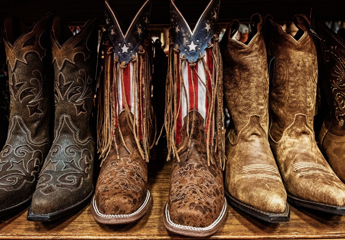 Plusieurs paires de bottes de cowboy en cuir aux motifs variés alignées sur une étagère, une paire arborant un motif de drapeau américain.