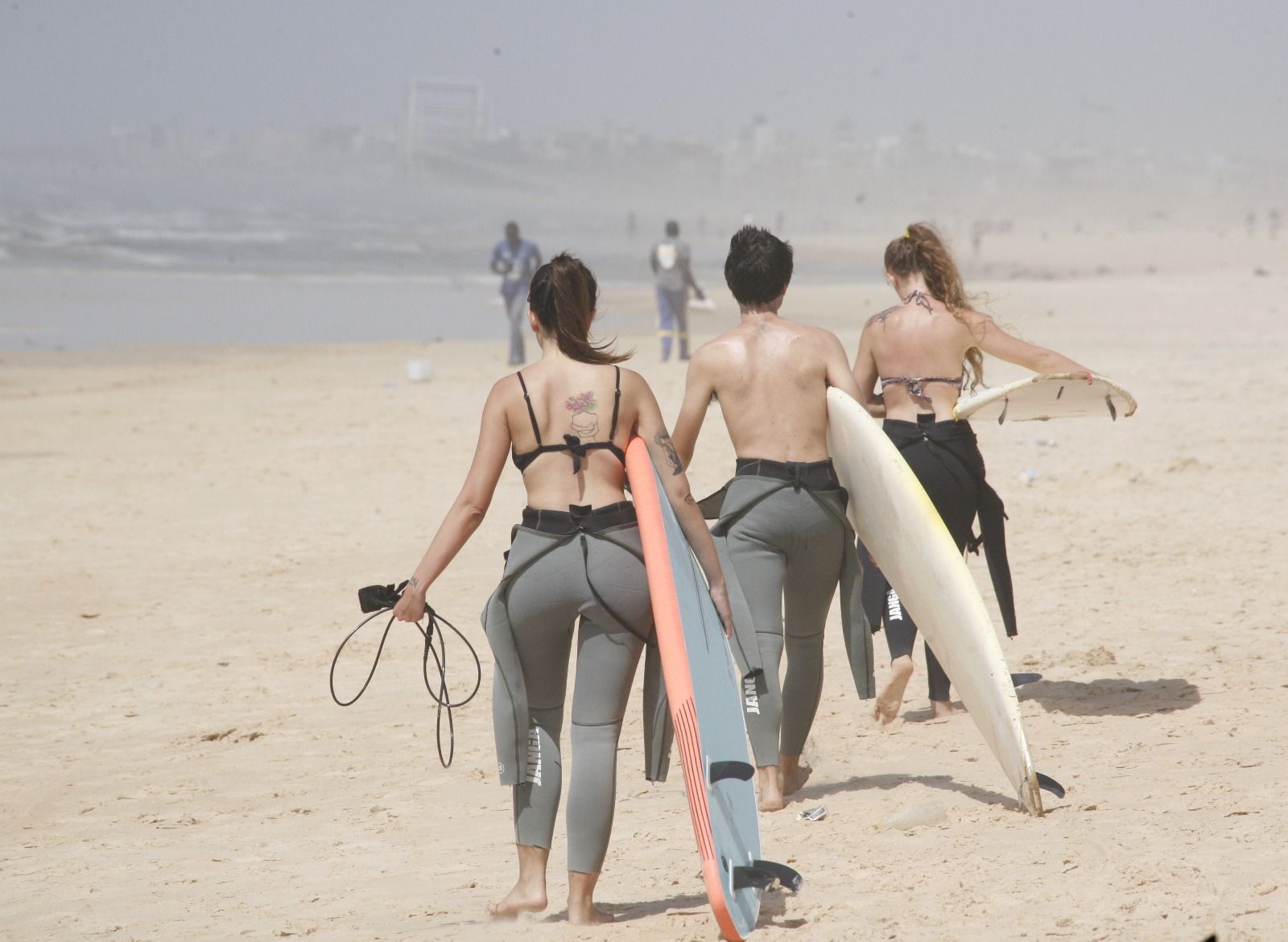 Un viaggio di gruppo WeRoad con tre persone in mute che camminano su una spiaggia sabbiosa con le loro tavole da surf verso l'acqua.