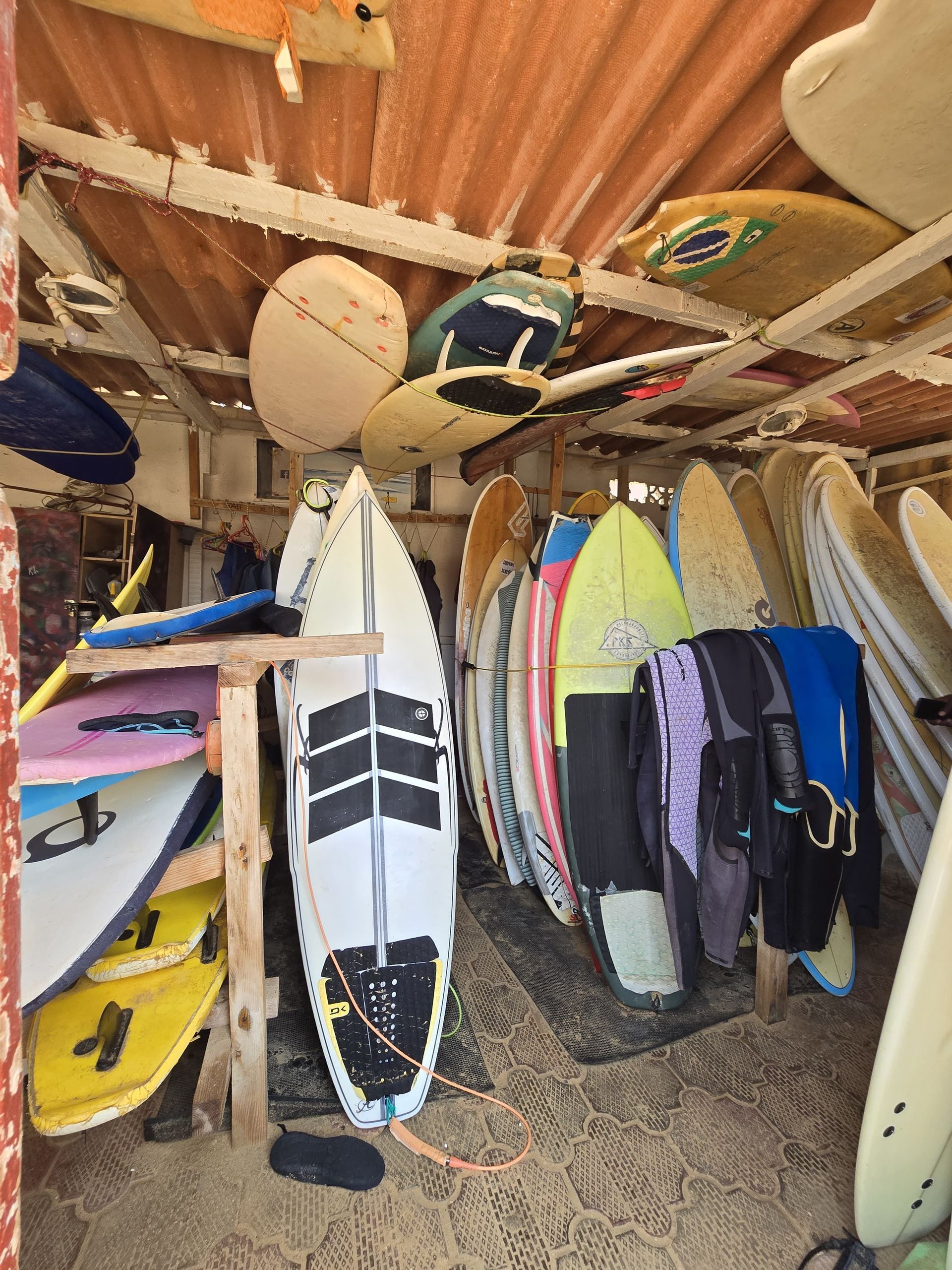 Decine di tavole da surf e mute riposte su rastrelliere e appese al soffitto di un rustico capanno da surf.