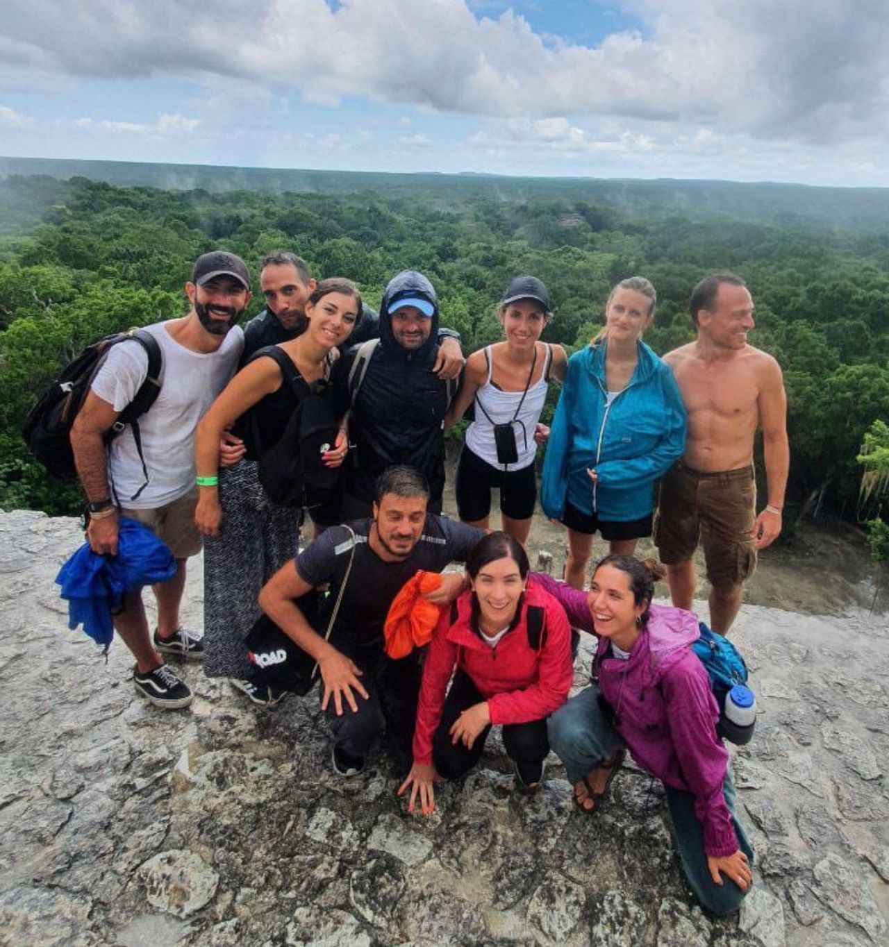 Un gruppo WeRoad in viaggio posa per una foto su un punto panoramico roccioso, con una vasta foresta verde che si estende sotto un cielo nuvoloso.
