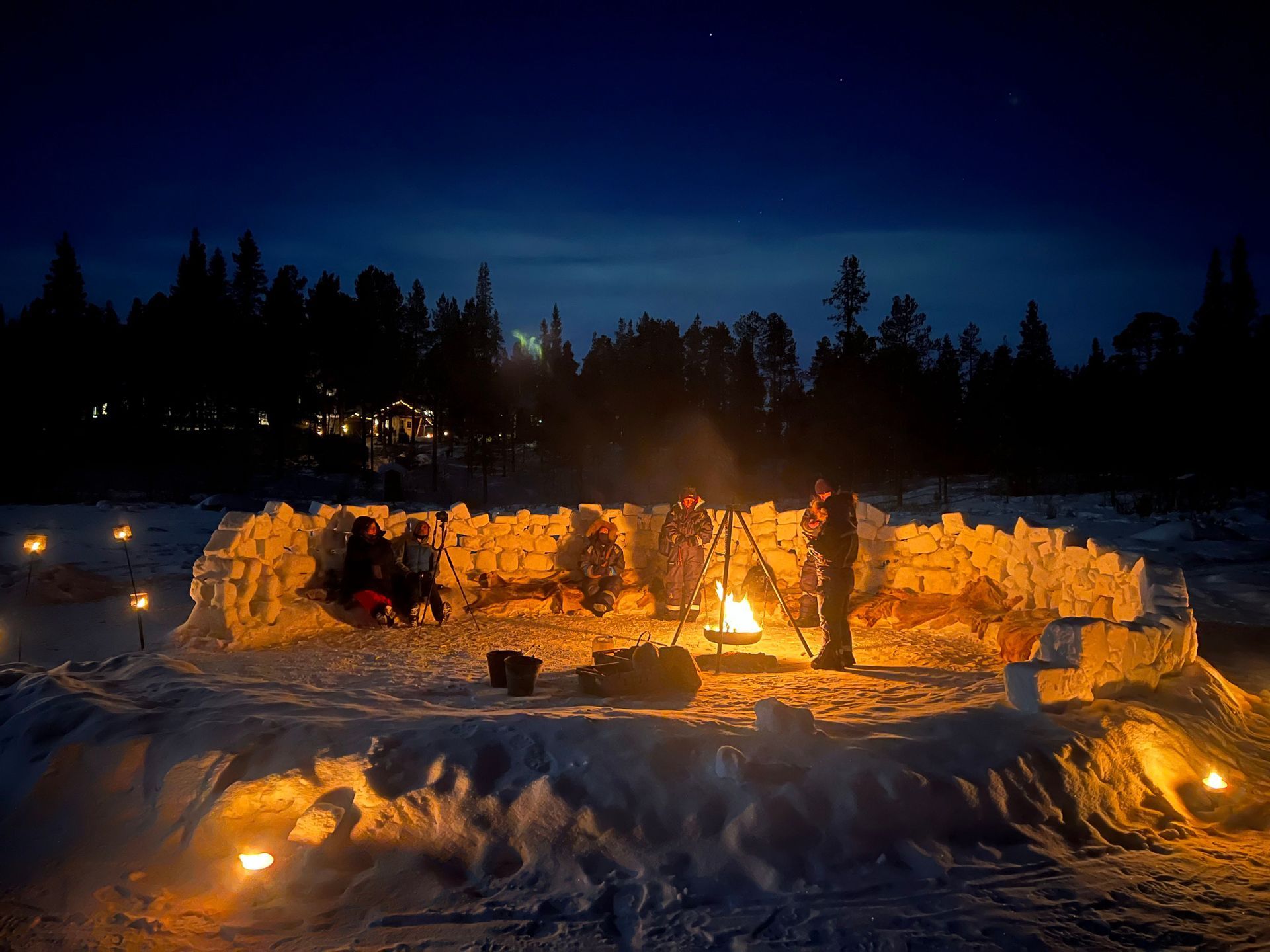 Un viaggio di gruppo WeRoad riunito attorno a un falò di notte in un paesaggio innevato, seduto all'interno di un muro circolare fatto di blocchi di neve.