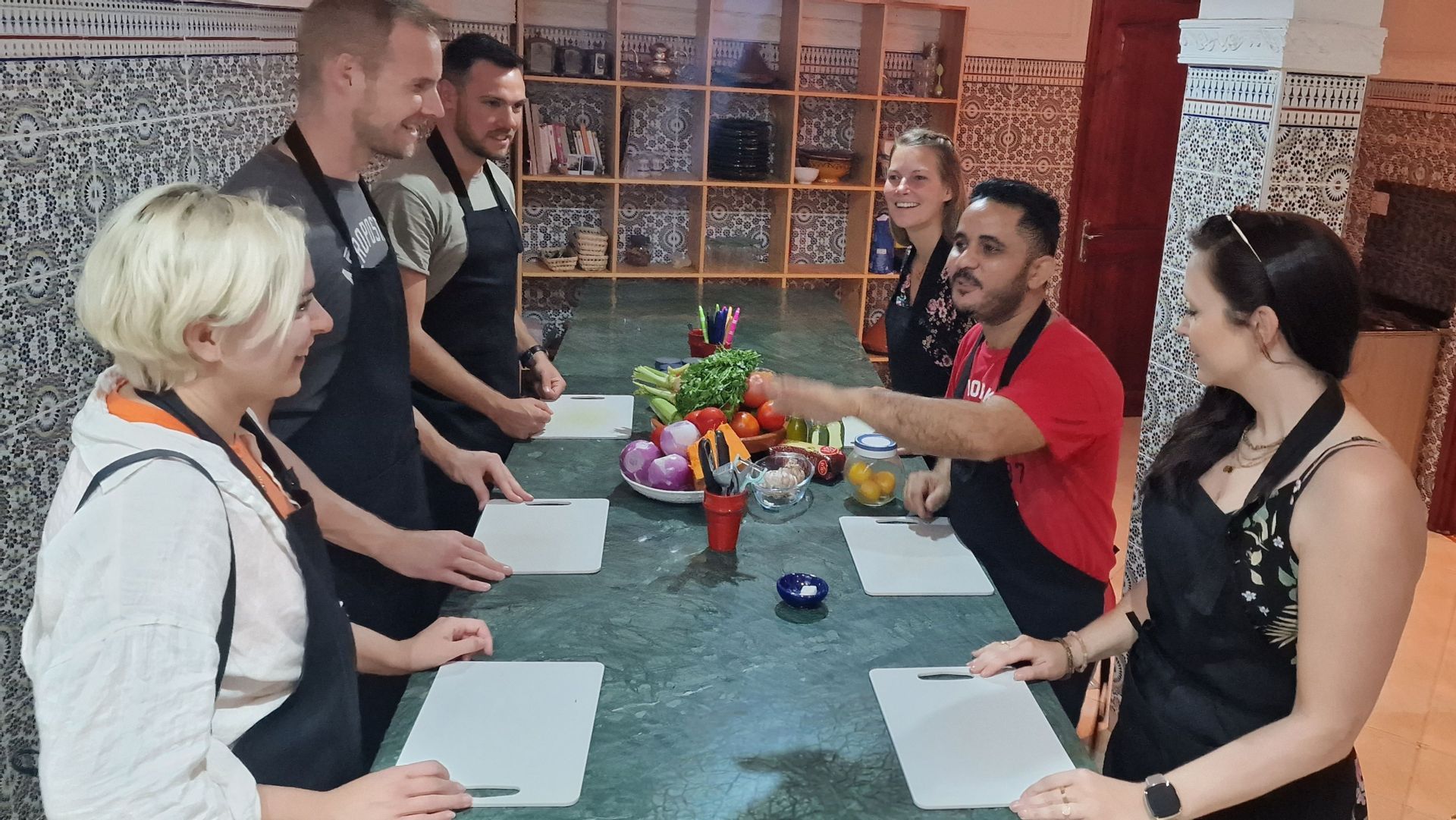 Eine WeRoad-Gruppe nimmt an einem Kochkurs teil, versammelt an einem großen Tisch mit frischem Gemüse und einem Kochlehrer.