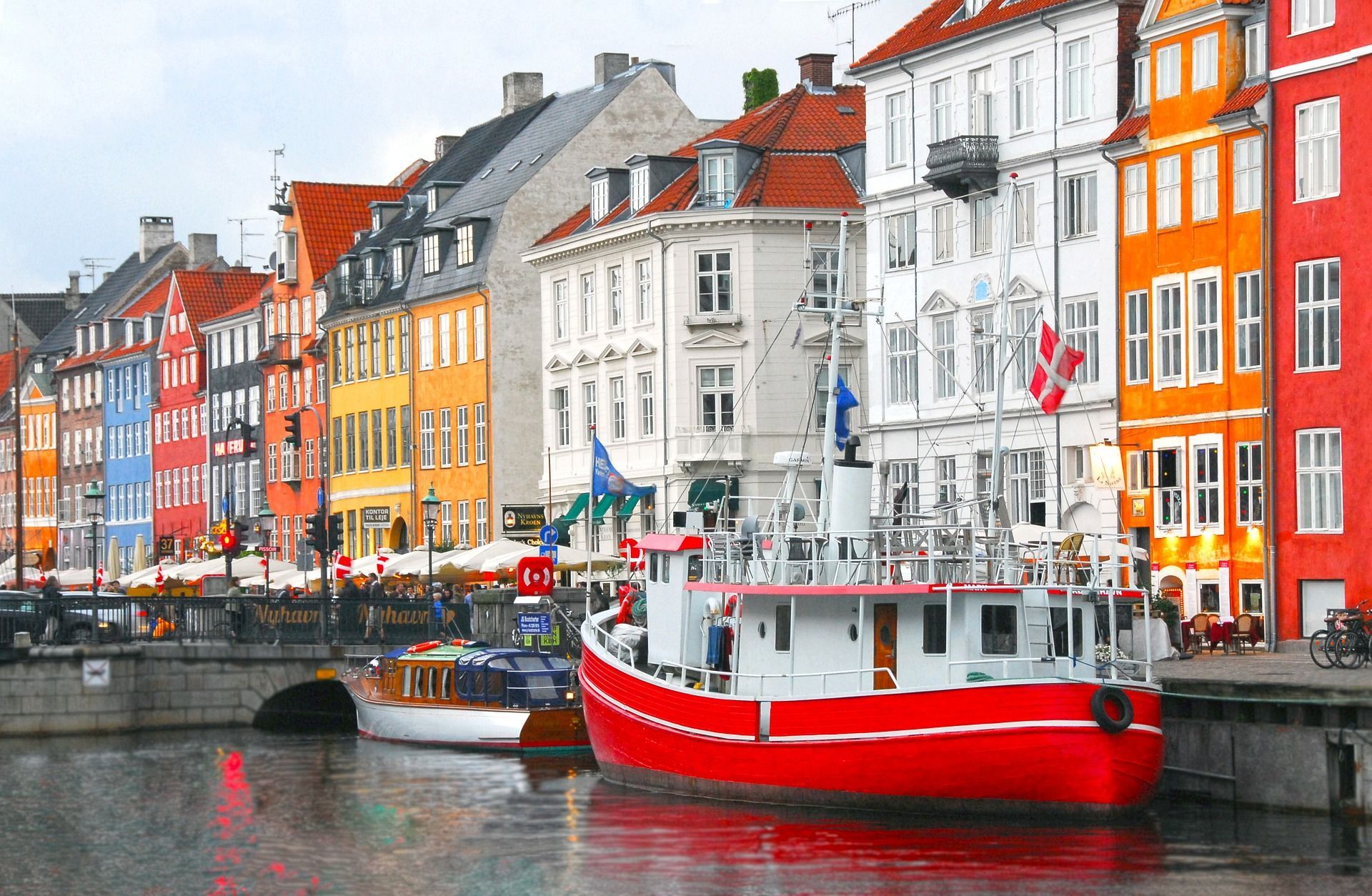 Una grande barca rossa è ormeggiata in un canale, con colorati edifici sul lungomare e un piccolo ponte sullo sfondo.
