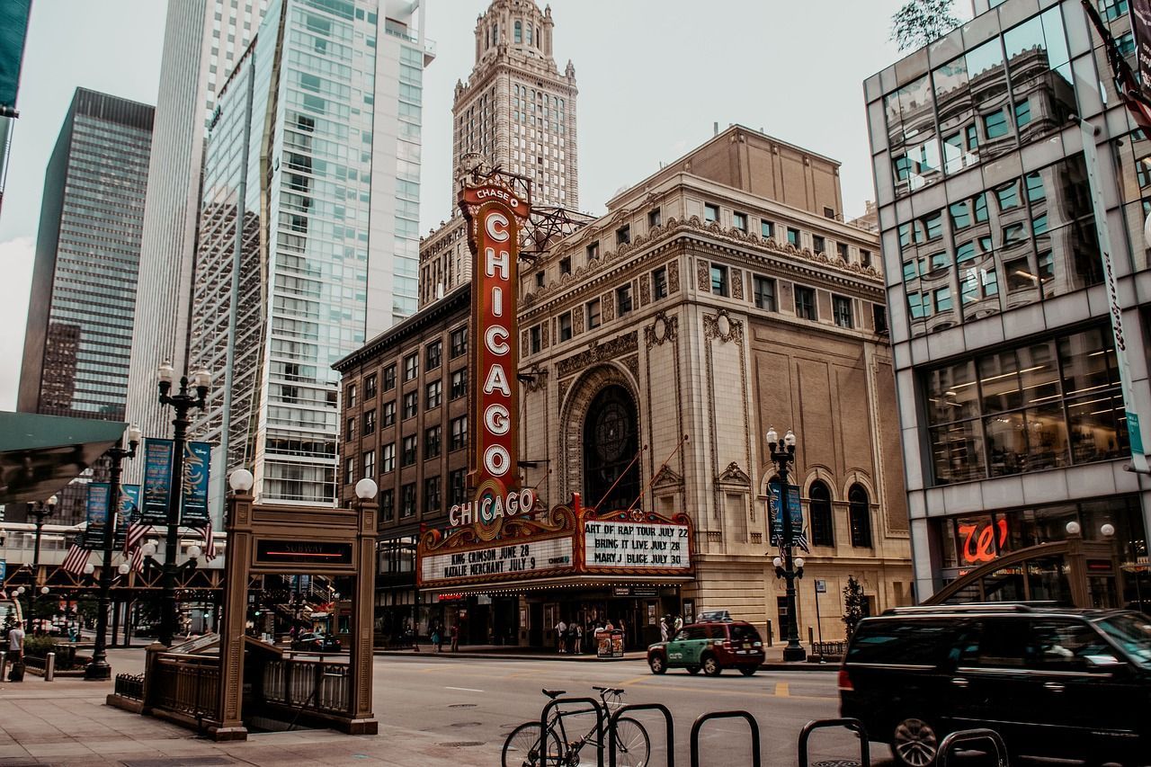 Una vista a nivel de calle del Teatro Chicago con su prominente letrero vertical, con un telón de fondo de rascacielos modernos y tráfico urbano.