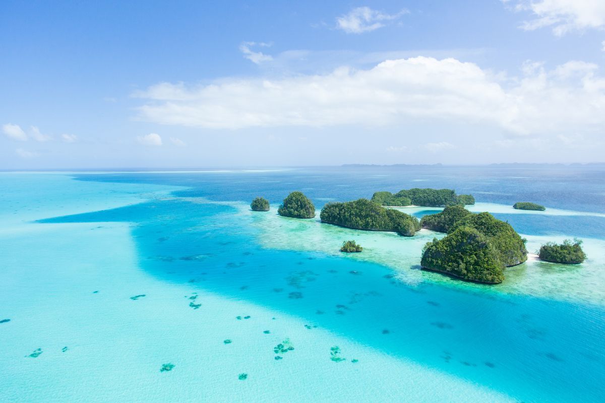 Una vista aerea di piccole isole rocciose coperte di vegetazione verde, sparse in un oceano turchese e blu intenso sotto un cielo parzialmente nuvoloso.