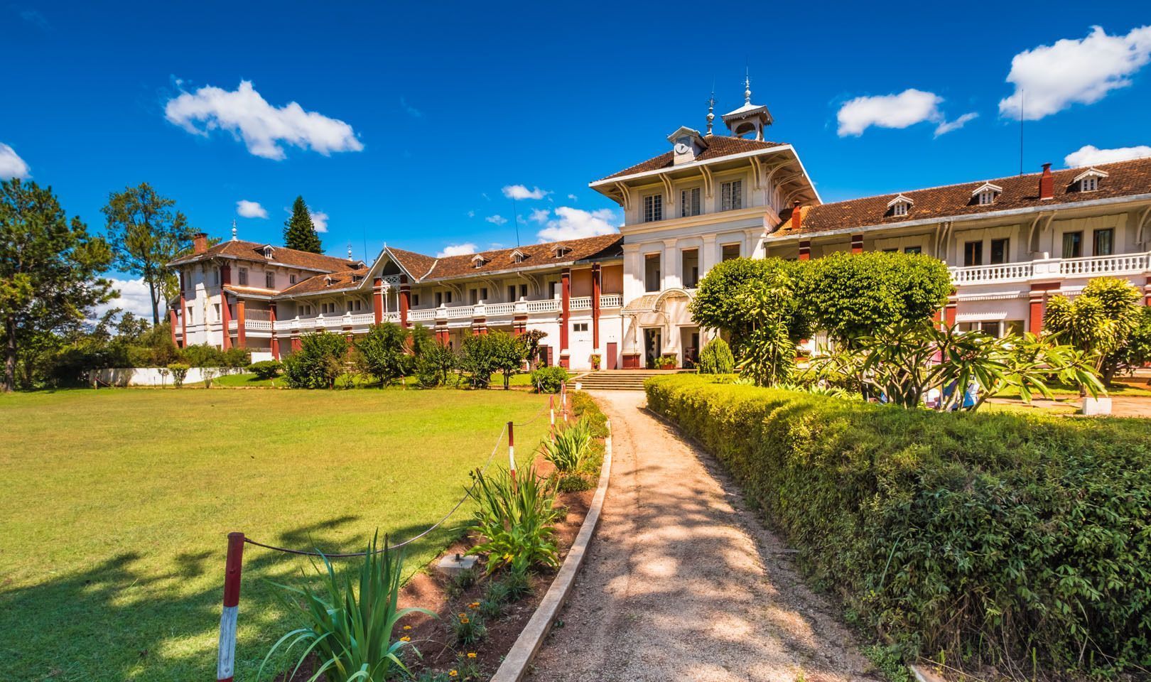 Ein Schotterweg führt durch einen gepflegten grünen Rasen zu einem großen Gebäude im Kolonialstil unter einem strahlend blauen Himmel.