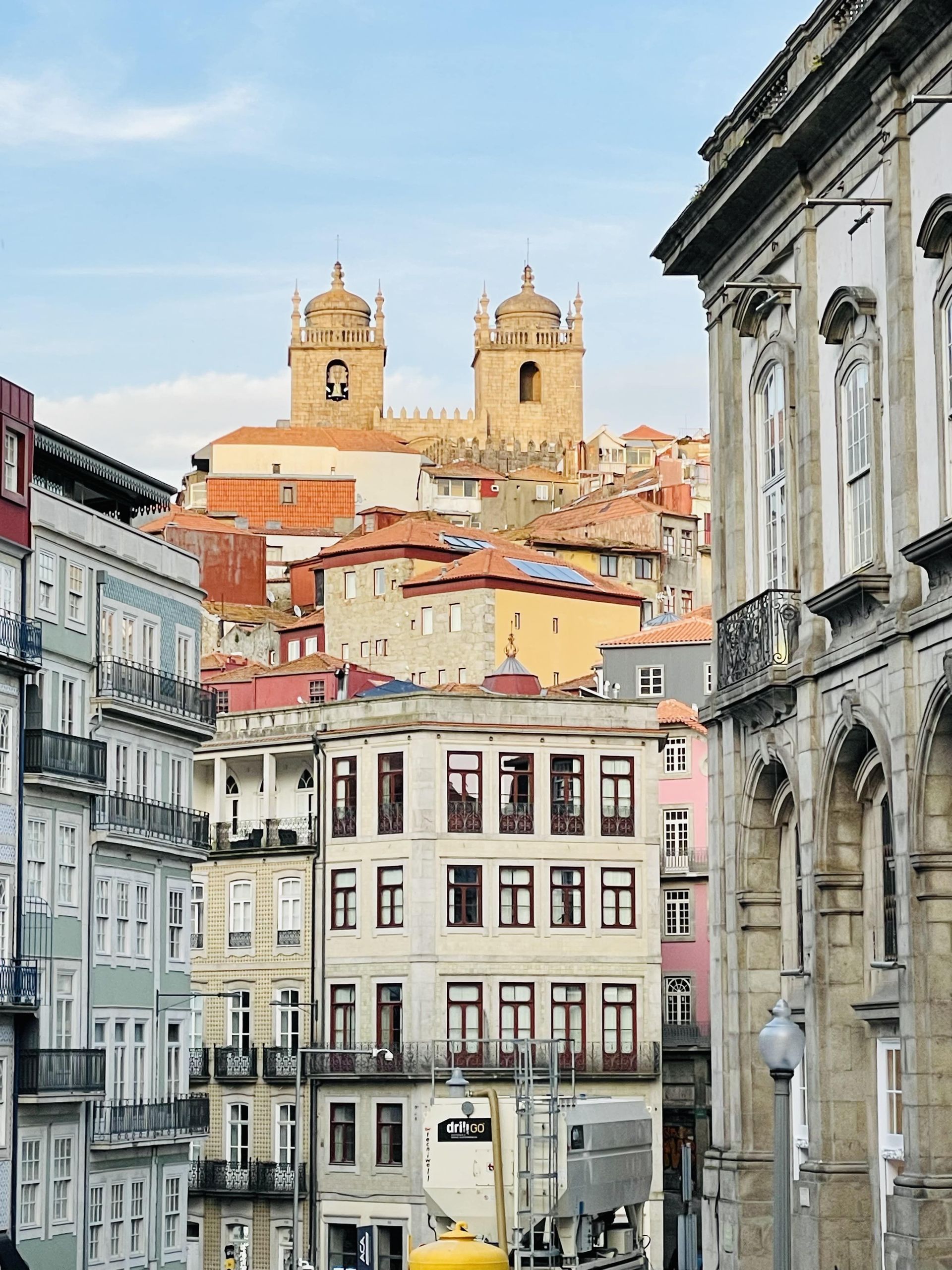 Una vista di edifici colorati della città che portano a una cattedrale in pietra con due campanili su una collina contro un cielo blu.