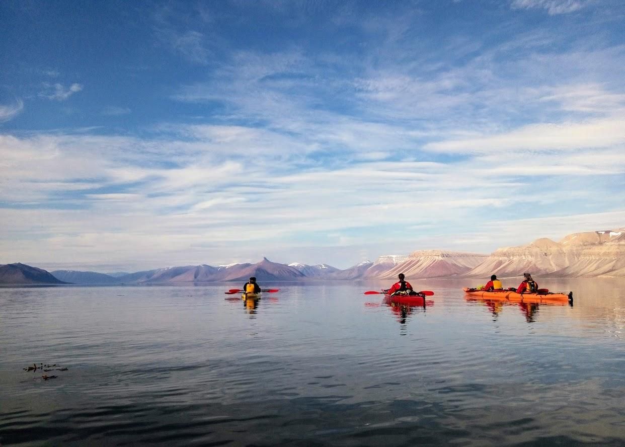 Un viaggio di gruppo WeRoad in kayak su acqua calma con montagne innevate sullo sfondo sotto un cielo blu.