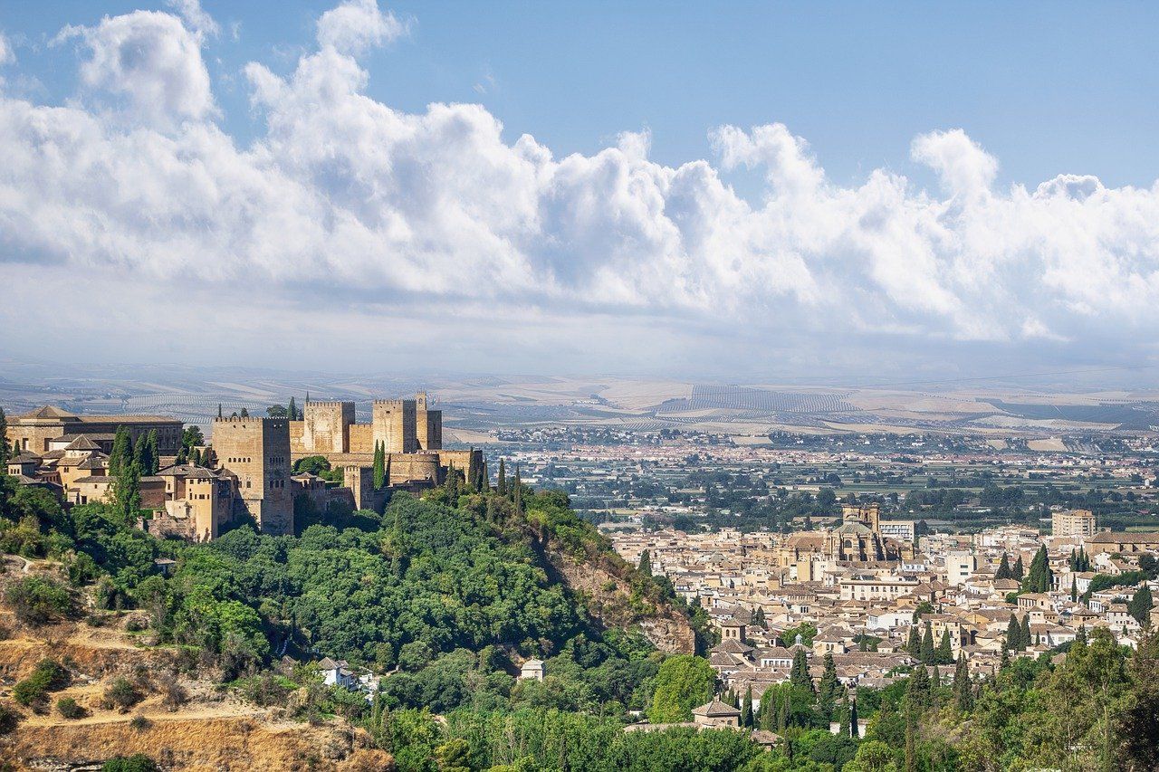 Una fortaleza histórica en una exuberante colina verde domina una ciudad en expansión y llanuras distantes bajo un cielo nublado.