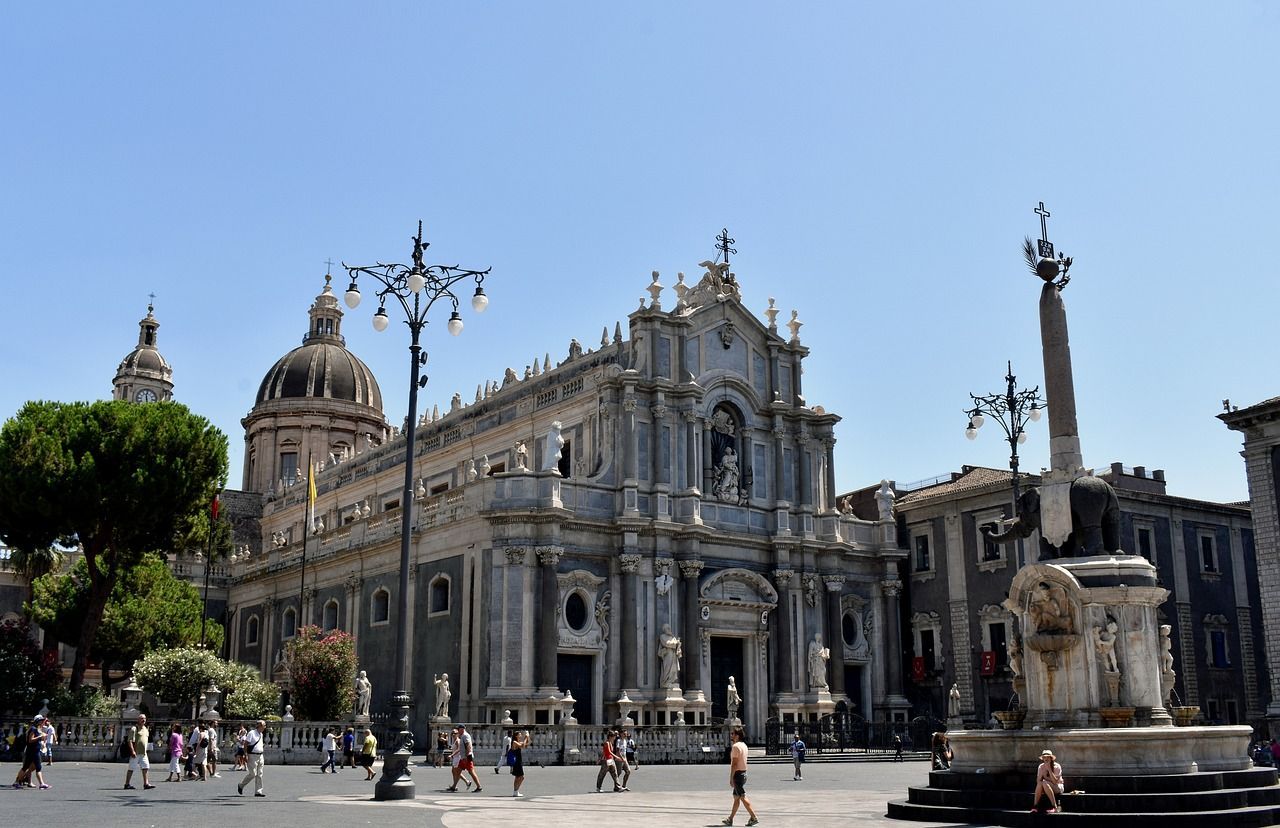 Una cattedrale barocca con una cupola e una fontana con una statua di elefante si ergono in una piazza storica in una giornata di sole.