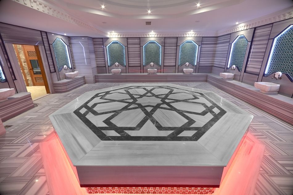 El interior de un moderno hammam turco con una gran plataforma octogonal de mármol decorada con un patrón geométrico en el centro.