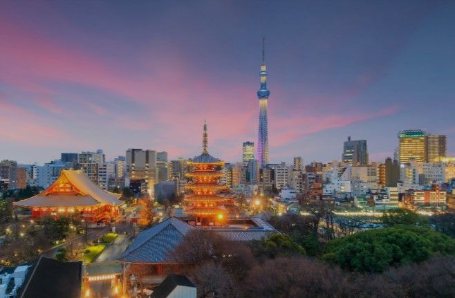 Un paesaggio urbano con pagode tradizionali illuminate e una torre moderna contro un cielo crepuscolare colorato.