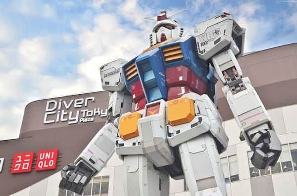 Uno scatto dal basso della statua gigante del robot Gundam di fronte all'edificio DiverCity Tokyo Plaza, sotto un cielo parzialmente nuvoloso.