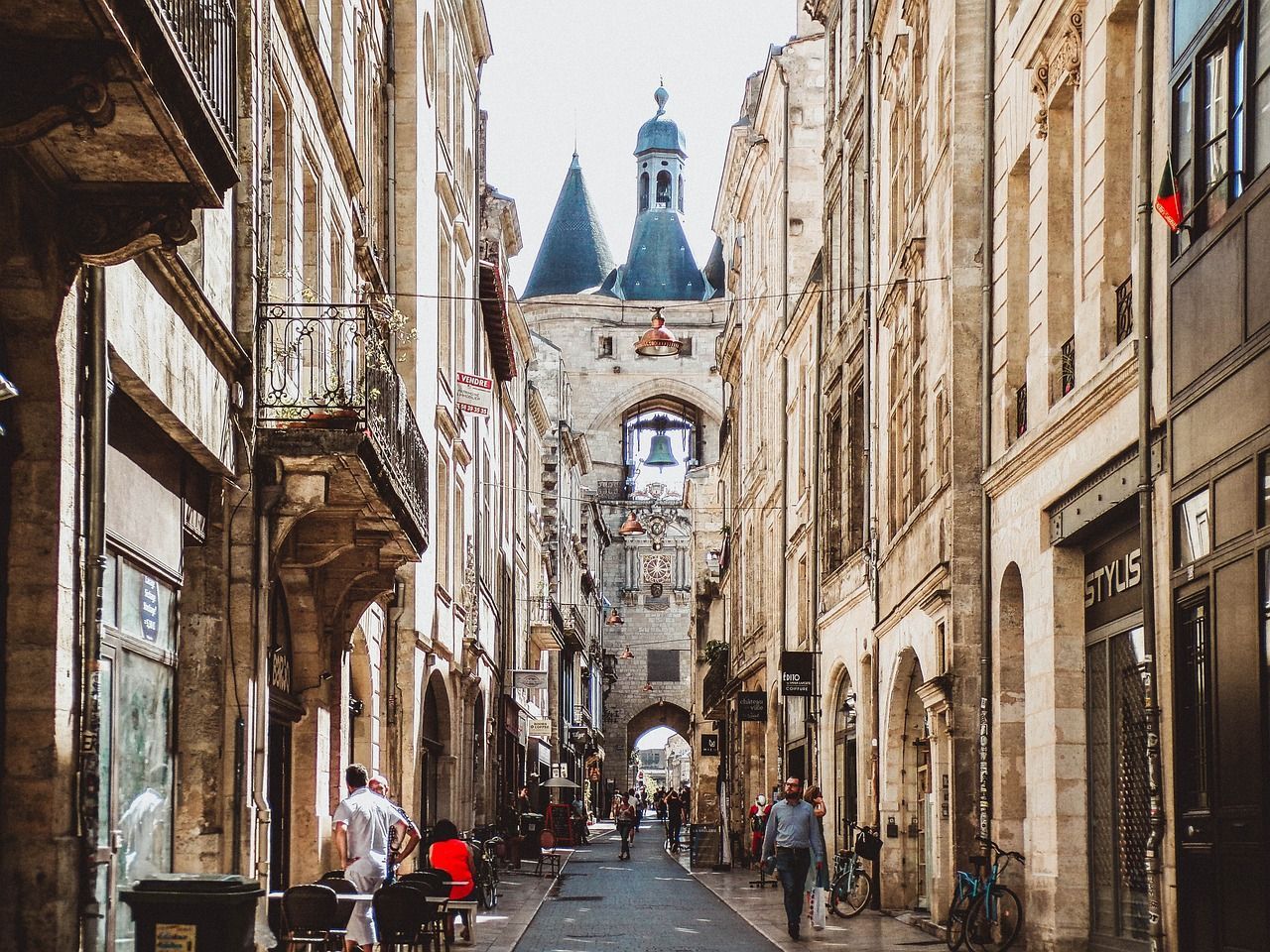 Una calle estrecha de adoquines en una ciudad europea, con gente caminando hacia un gran campanario a lo lejos.