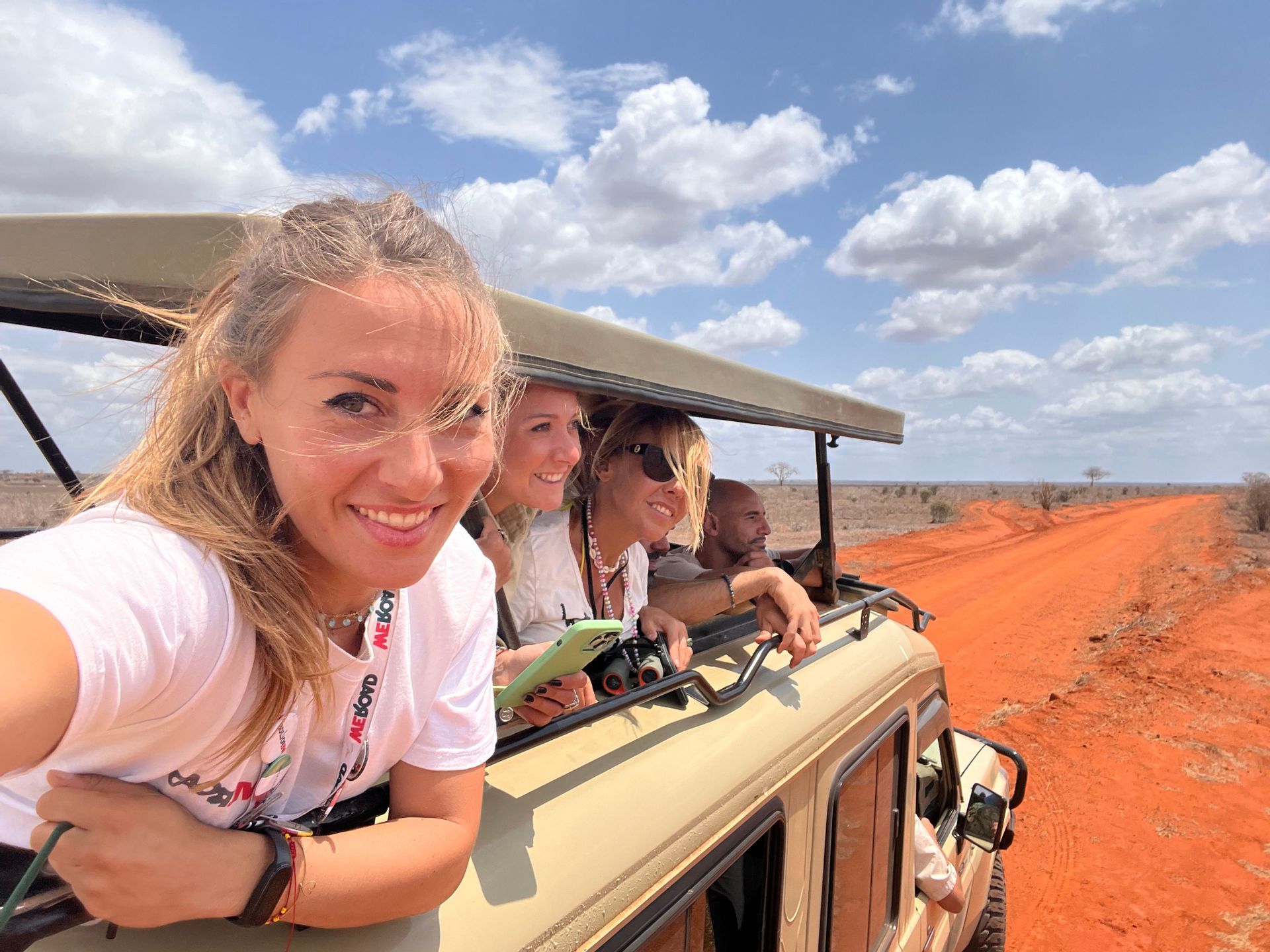Un gruppo WeRoad scatta un selfie da un veicolo safari scoperto su una strada sterrata rossa nella savana.