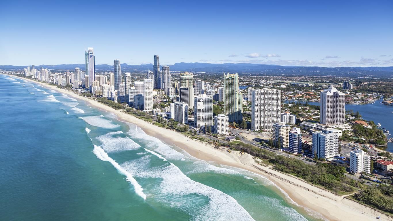 Una vista aérea del horizonte de una ciudad con rascacielos a lo largo de una larga playa de arena junto a un océano turquesa con olas blancas.