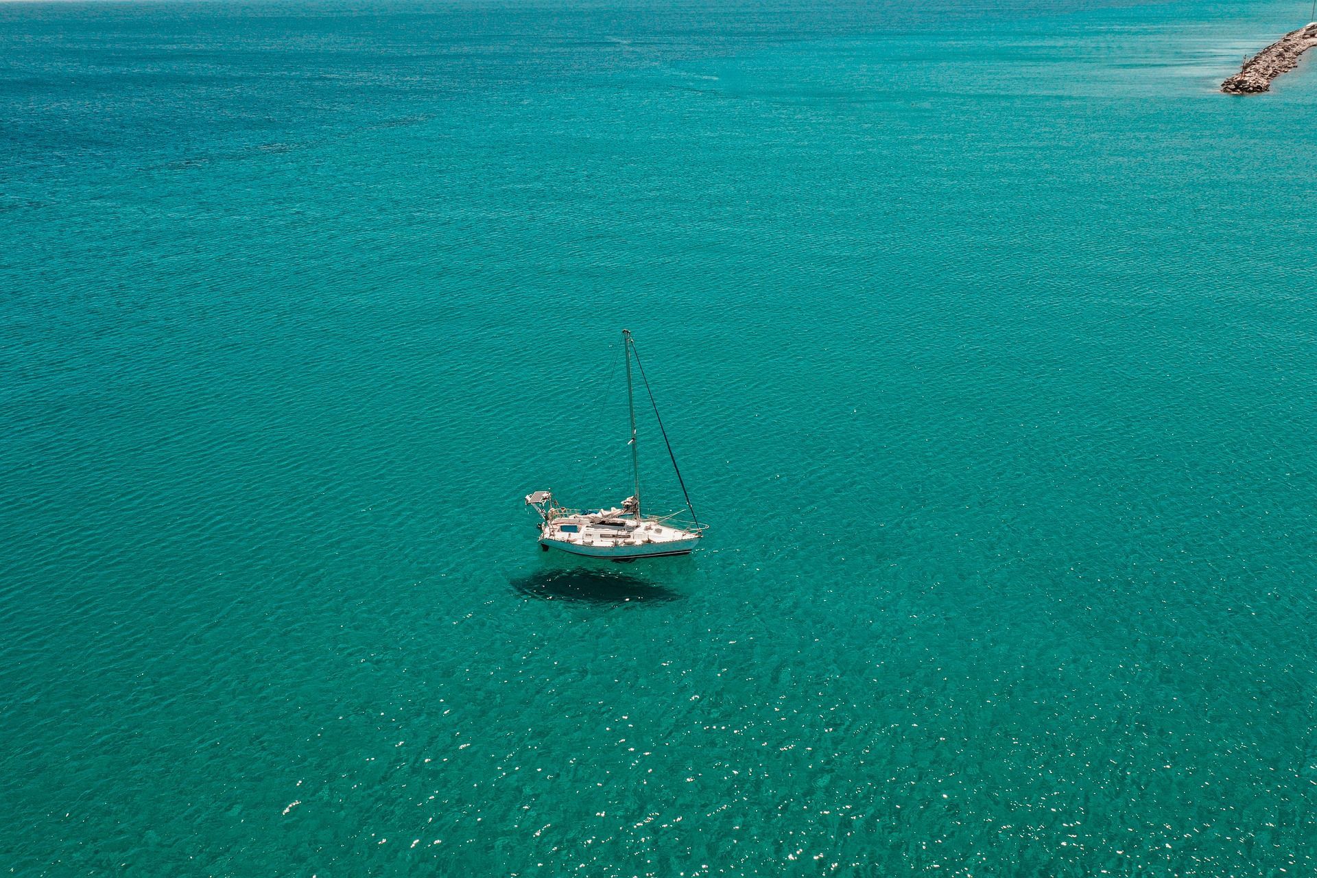 Una vista aerea di una barca a vela bianca che galleggia sola su un vasto, calmo mare turchese.