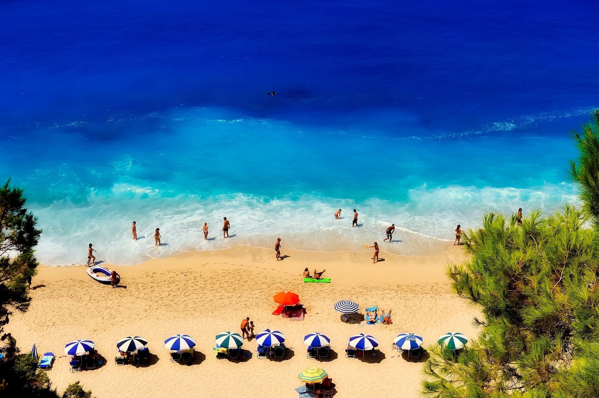 Una vista dall'alto di persone che si rilassano su una spiaggia sabbiosa con ombrelloni colorati vicino ad acque turchesi e blu profondo.