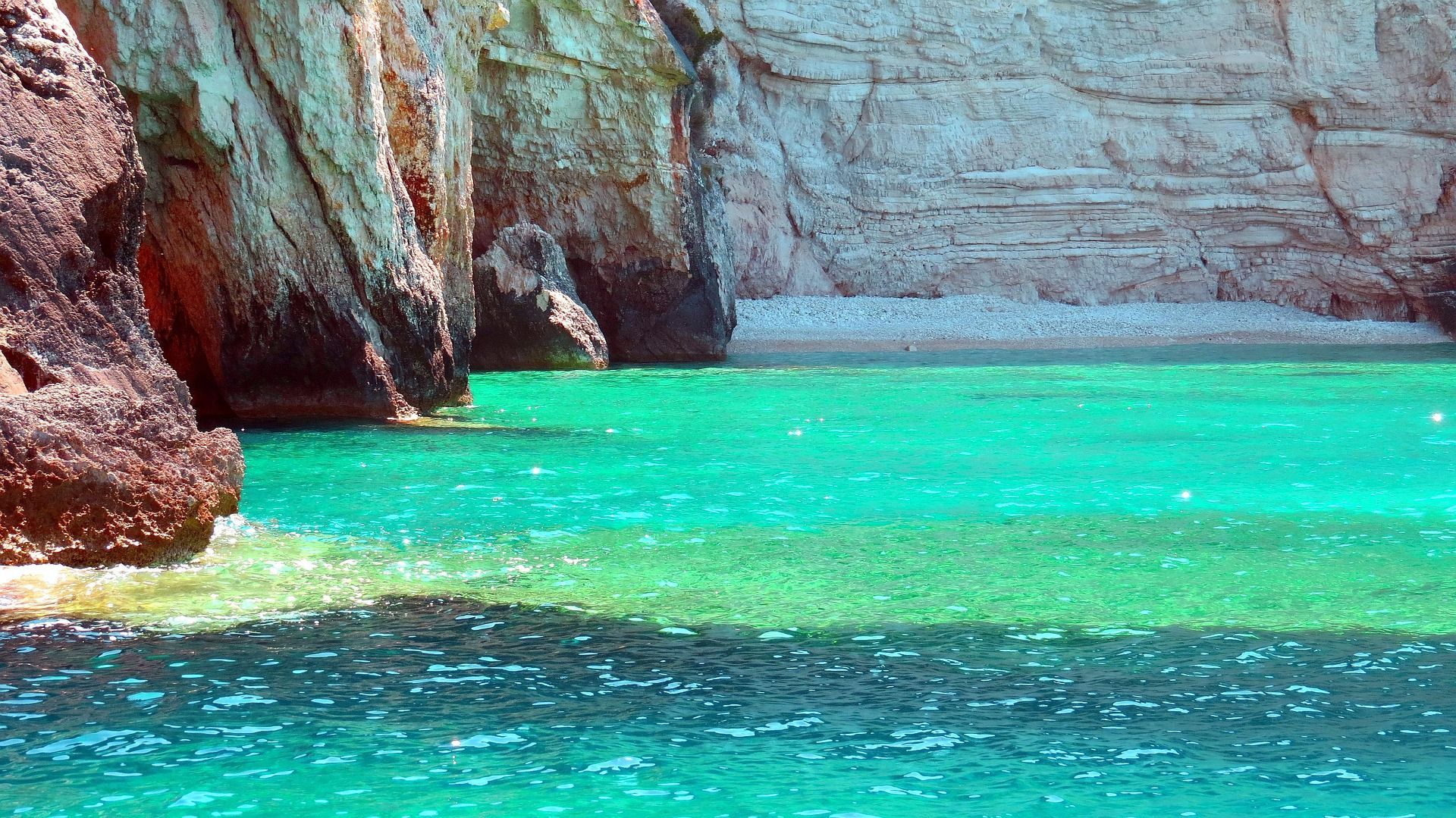 Acque turchesi e vibranti del mare incontrano la base di alte scogliere rocciose che costeggiano una spiaggia di ciottoli appartata.