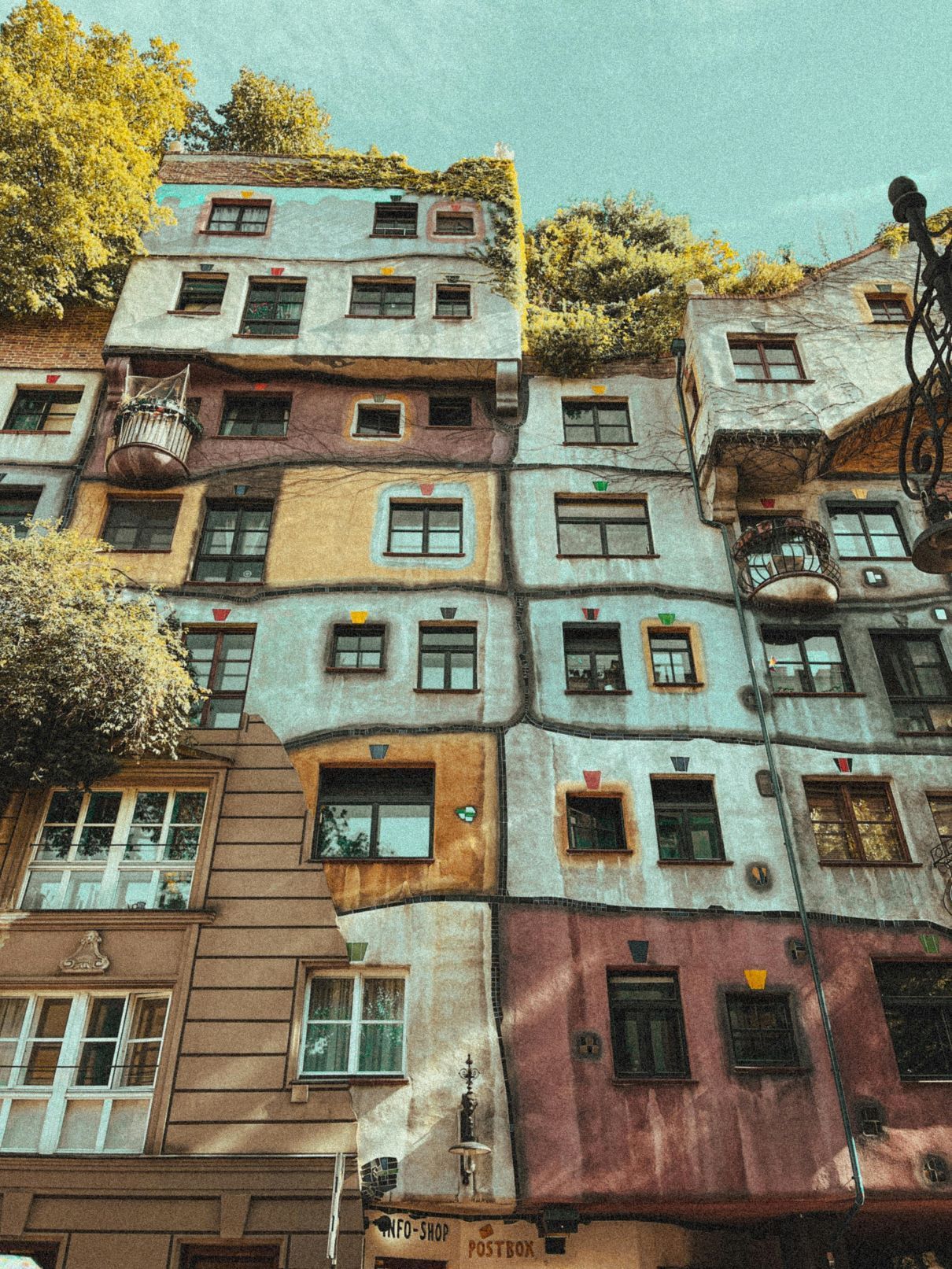 Una vista dal basso di un edificio multicolore con facciata irregolare, finestre non allineate e alberi sul tetto.