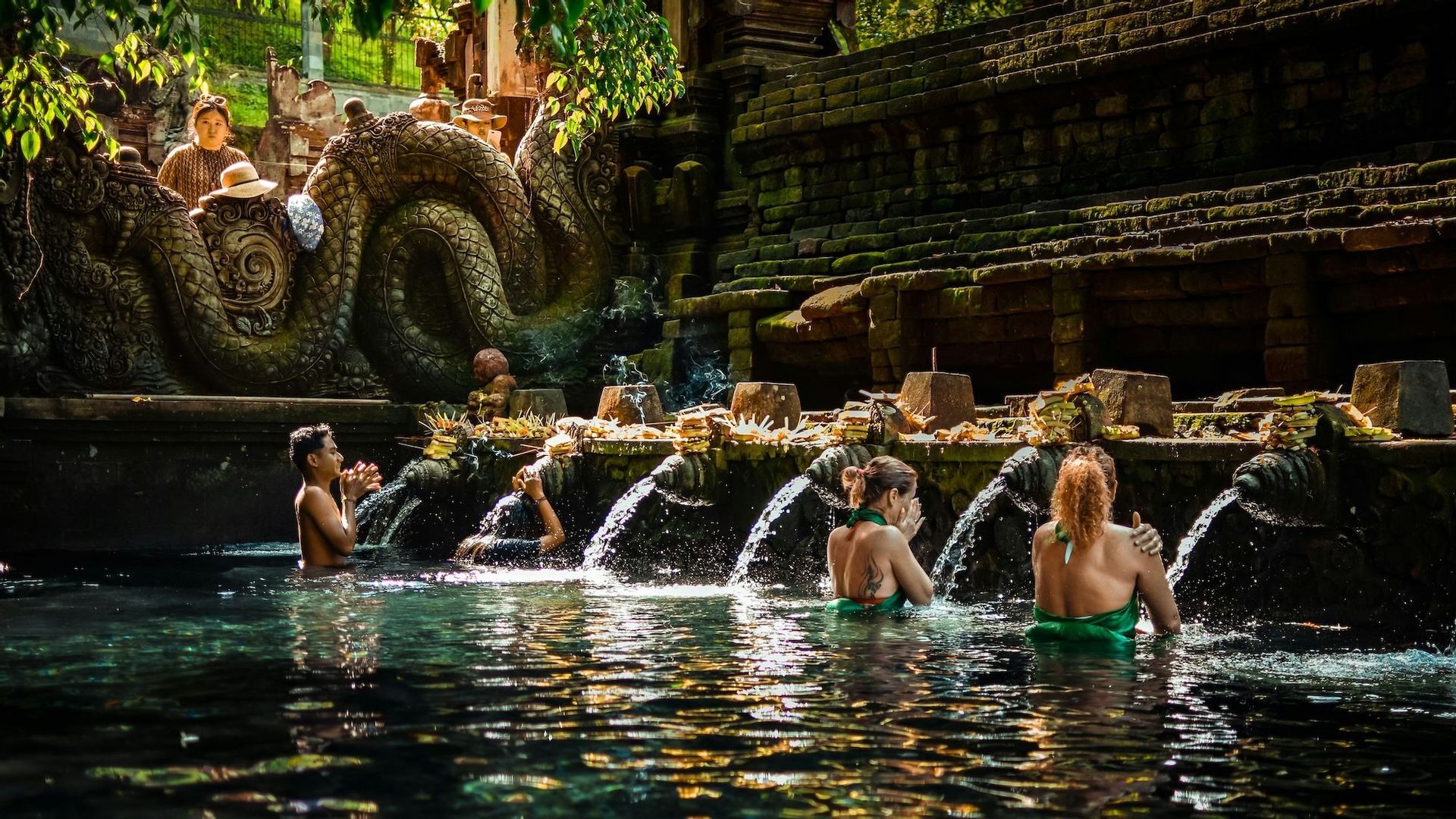 Un viaggio di gruppo WeRoad esegue un rituale di purificazione dell'acqua, lavandosi sotto le bocche di pietra di un tempio.