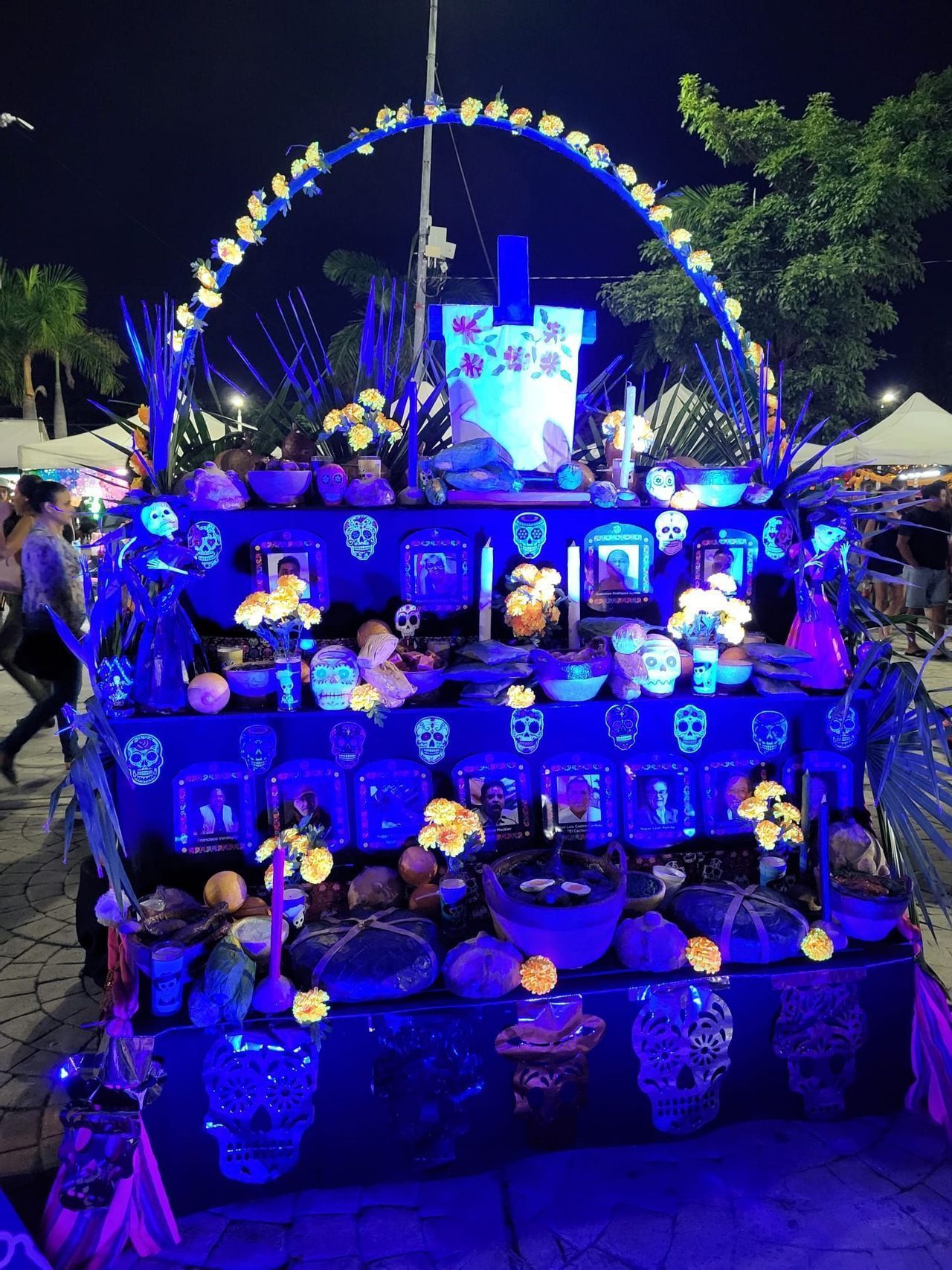 Un tradizionale altare ofrenda del Giorno dei Morti illuminato da luci blu di notte, decorato con teschi, fiori e foto incorniciate.