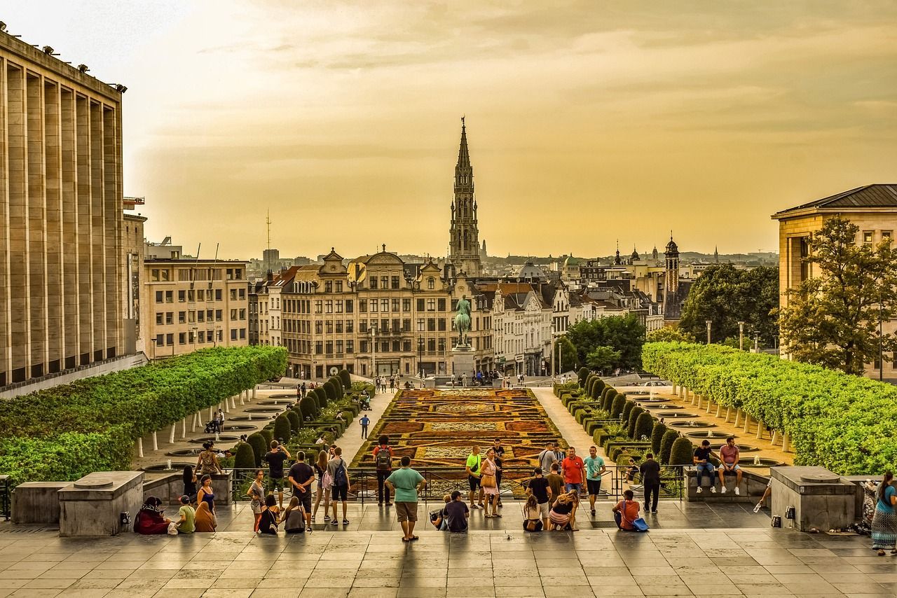 Un gruppo di persone su scalini di pietra che si affaccia su un giardino formale con un grande tappeto floreale e uno skyline di città europea.