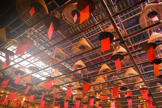 Una vista dal basso di numerose spirali di incenso coniche con etichette rosse, appese a un soffitto a griglia di legno.