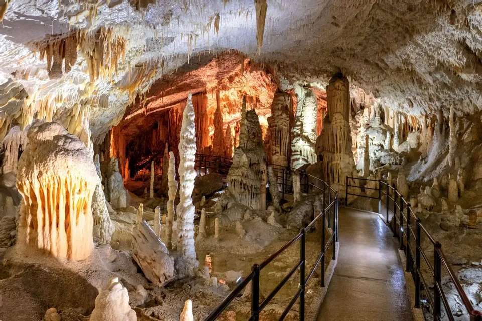 Un sendero pavimentado con pasamanos atraviesa una gran cueva iluminada con muchas estalactitas y estalagmitas.