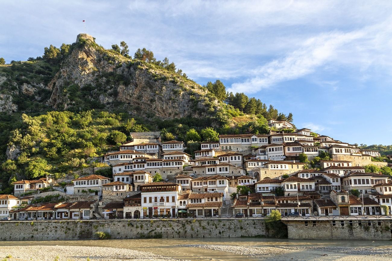 Casas de paredes blancas y tejados de tejas construidas en una exuberante ladera verde, con una fortaleza en la cima y un río debajo.