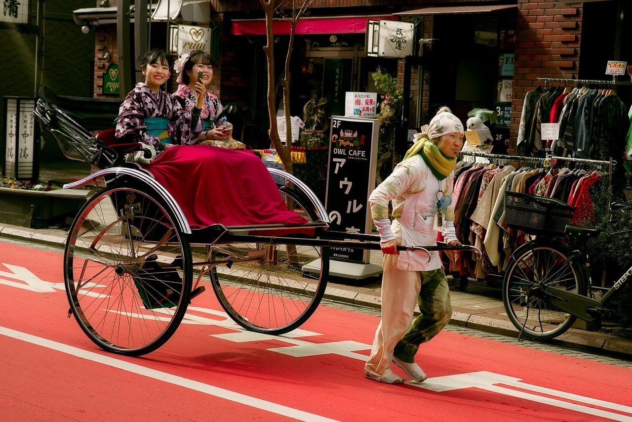Un hombre tira de un rickshaw que lleva a dos mujeres sonrientes vestidas con kimonos tradicionales por una calle de la ciudad pintada de rojo.