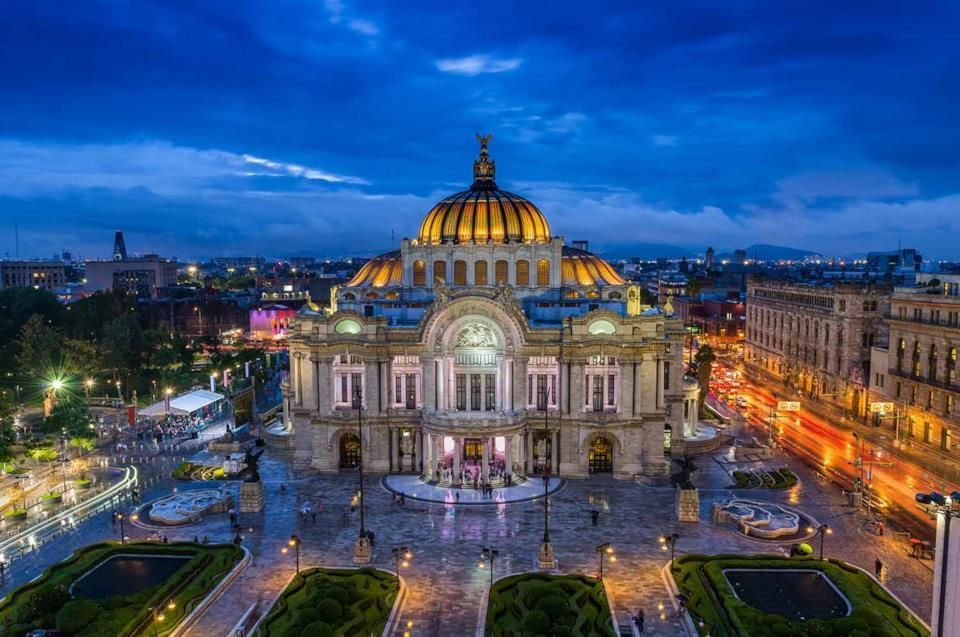 An ornate palace with a golden dome, brightly lit against a city skyline at dusk with gardens in the foreground.