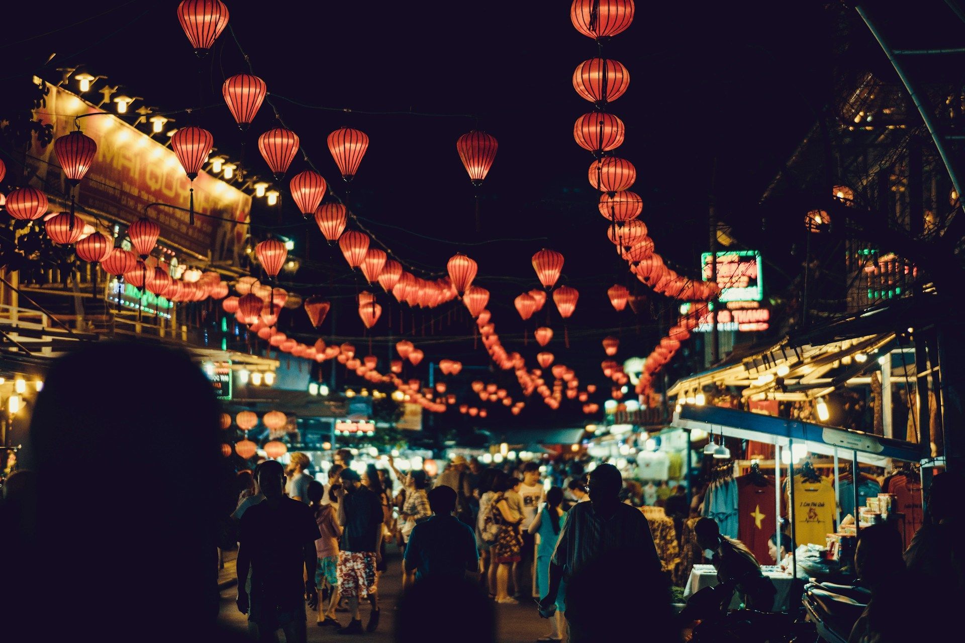 Lanterne rosse luminose pendono sopra un affollato mercato notturno.