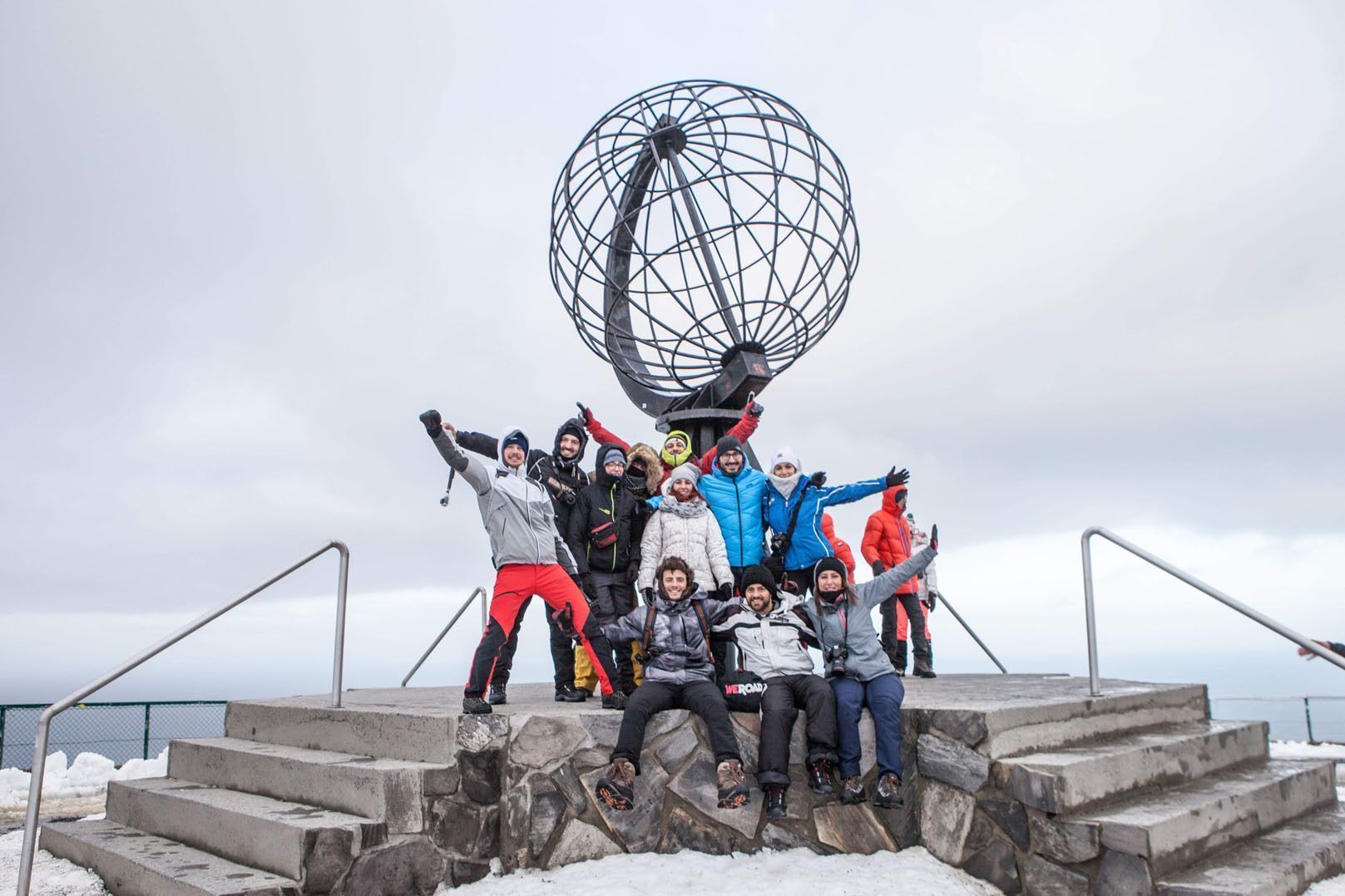Un grupo de viaje de WeRoad con ropa de invierno posando frente a una gran escultura de globo metálico sobre una plataforma de piedra nevada.