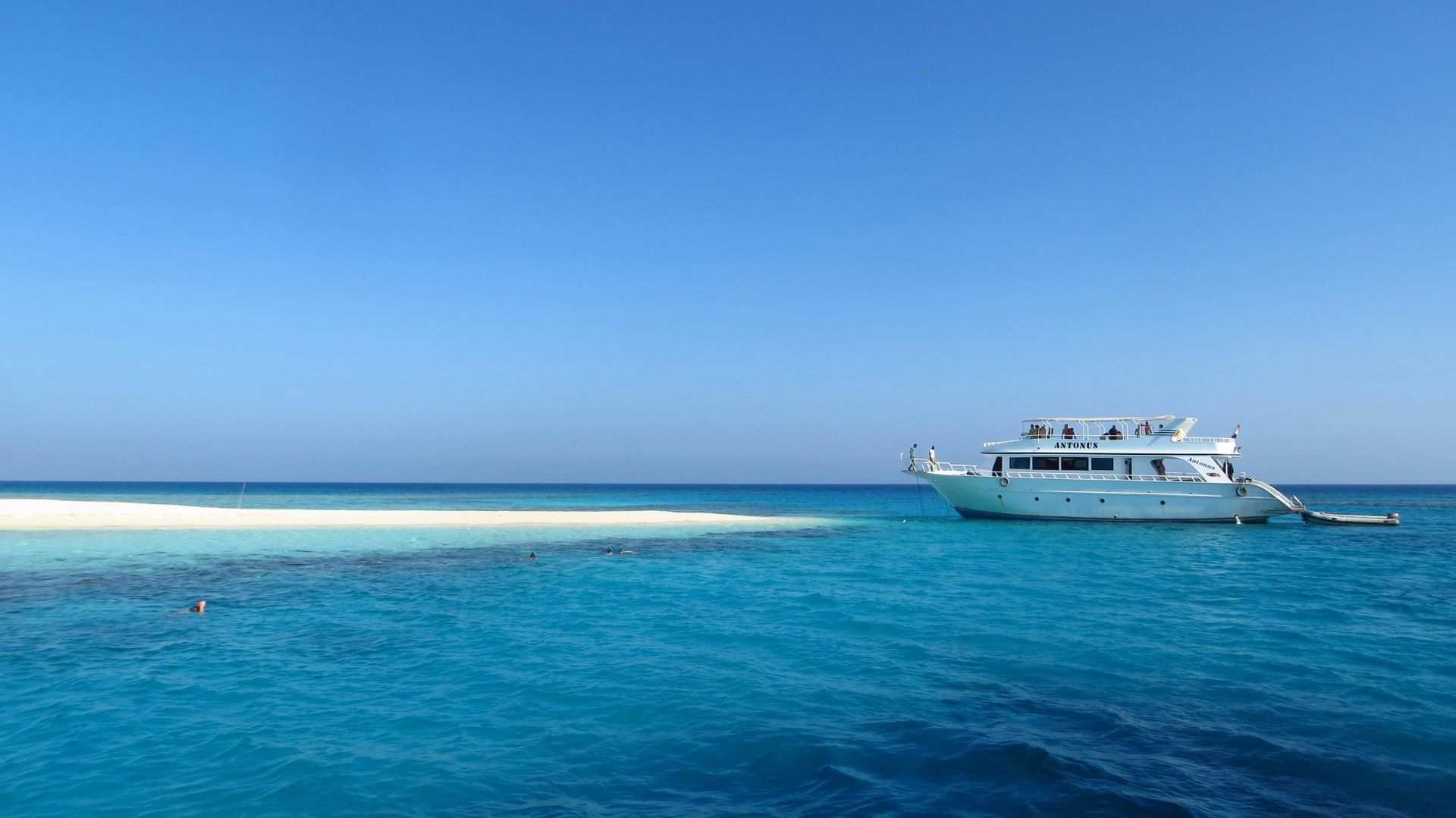Un viaje en grupo de WeRoad en un gran barco blanco anclado en agua turquesa junto a un banco de arena blanca bajo un cielo azul claro.