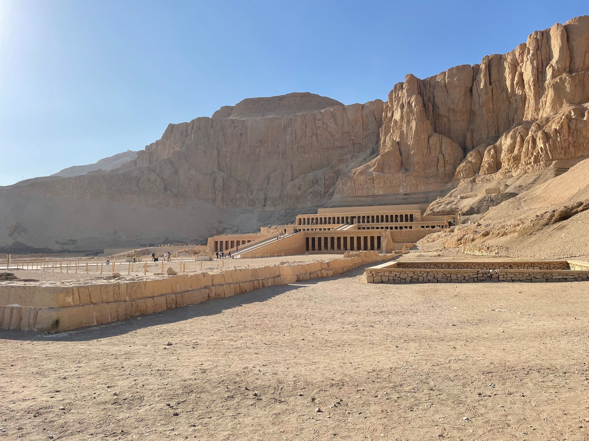 Un gran templo aterrazado con rampas y columnatas, construido en la base de un acantilado escarpado y rocoso en un paisaje desértico.