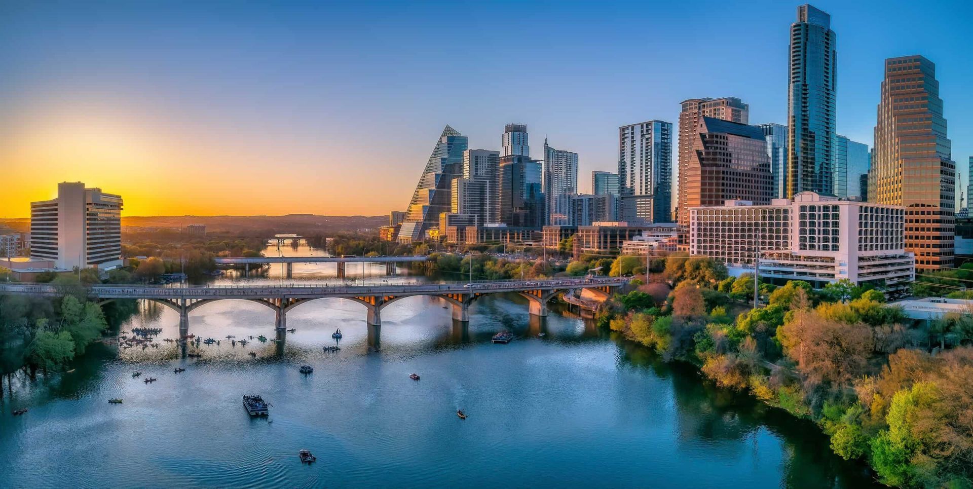 Vista aerea di uno skyline cittadino al tramonto, con un ponte su un fiume dove si pratica kayak.