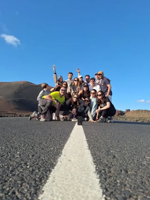 Un viaggio di gruppo WeRoad in posa per una foto su una strada deserta, con colline scure e un cielo azzurro chiaro sullo sfondo.