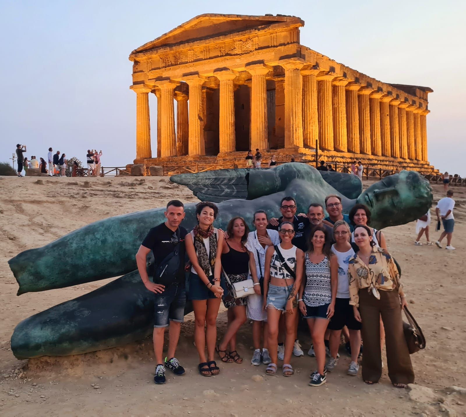 Un grupo de viaje de WeRoad posa para una foto frente a una gran estatua caída con un templo antiguo al fondo al atardecer.