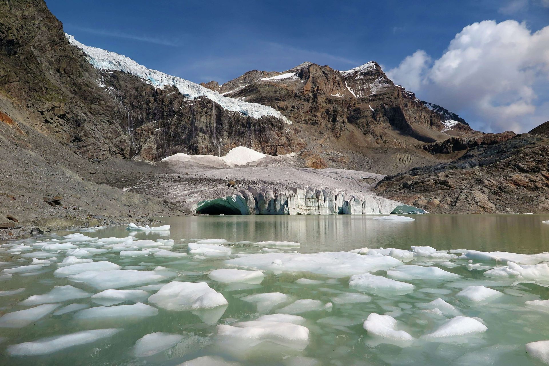 Un lago glaciale con iceberg galleggianti si trova di fronte a un enorme ghiacciaio incastonato tra montagne rocciose e coperte di neve.