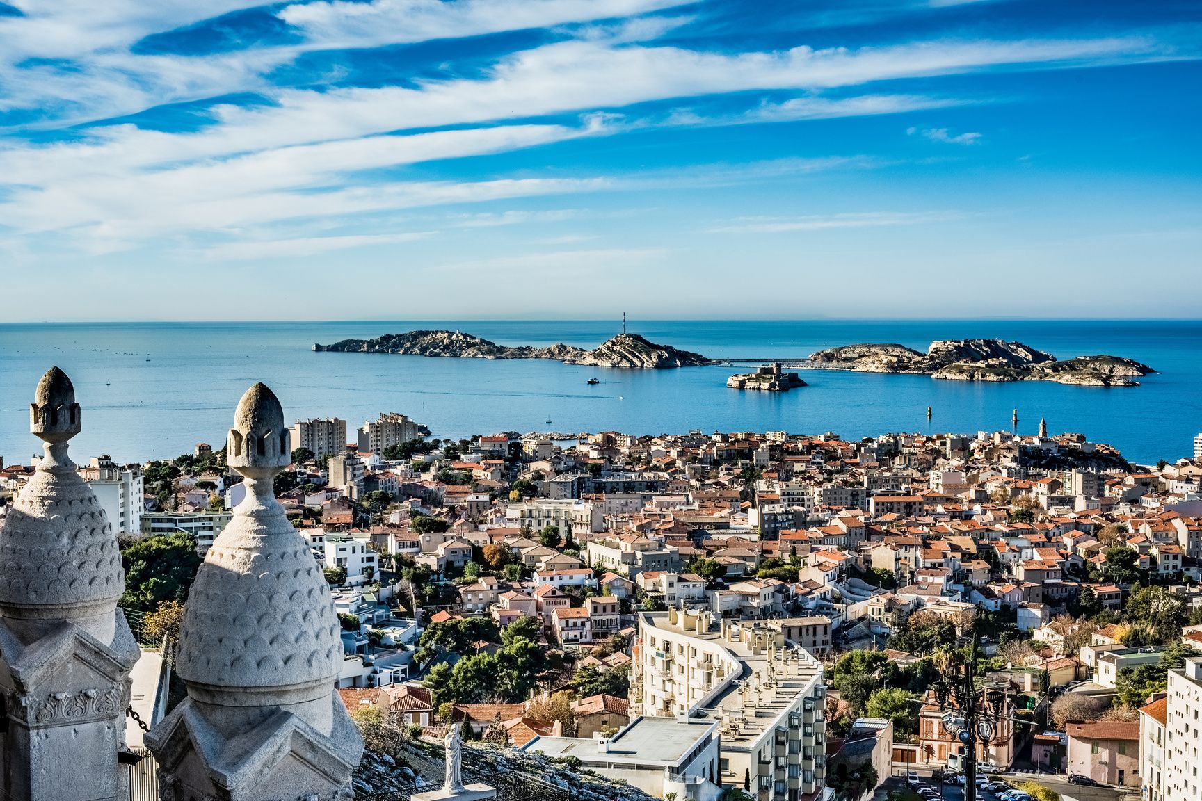 Una vista panorámica desde arriba de una ciudad costera con tejados de tejas rojas, con vistas a un mar azul con varias islas bajo un cielo brillante.