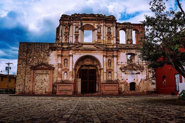 La facciata logora di una chiesa in pietra in rovina si erge dietro una piazza acciottolata sotto un cielo nuvoloso.